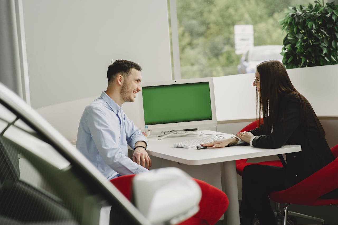 A man and woman engage in a business discussion in a modern office setting with a computer.